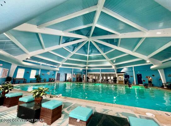 Indoor swimming pool beneath a turquoise ceiling with white beams and poolside lounge chairs.
