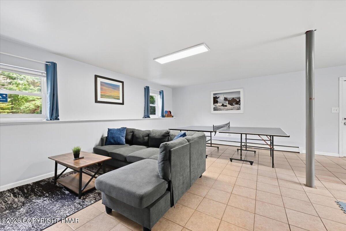 Recreation room with a gray sectional sofa and ping-pong table on tan tile flooring.