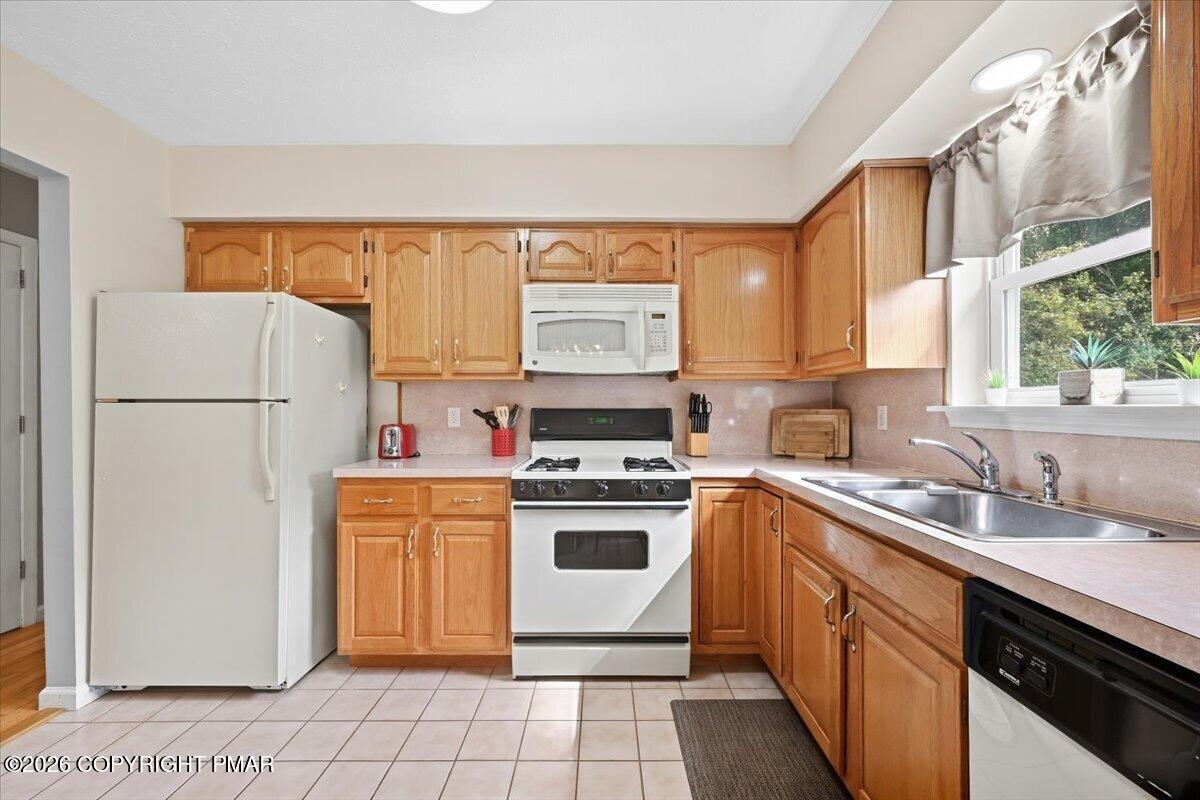 Kitchen with honey-colored cabinets, white appliances, and a double-basin sink beneath a large window.