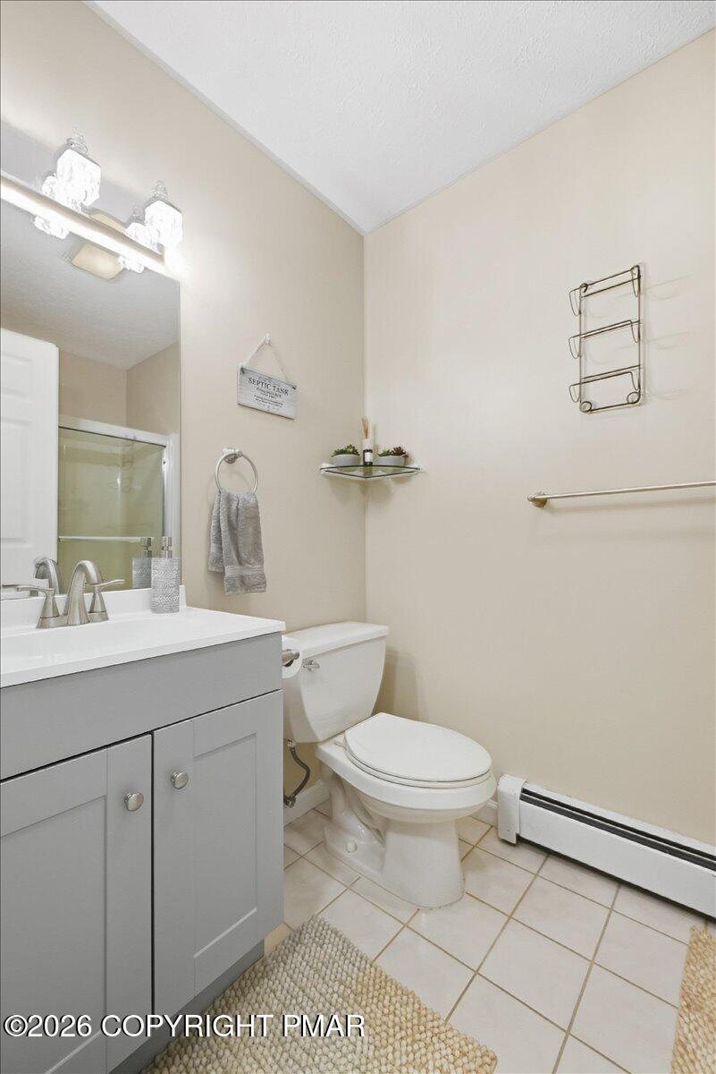 Bathroom with gray vanity, white toilet, tiled floor, and glass-enclosed shower.