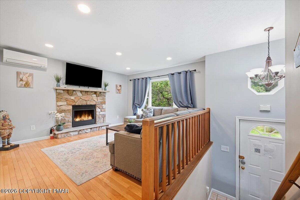 Living room with a stone fireplace, hardwood floors, and wooden stair railing.