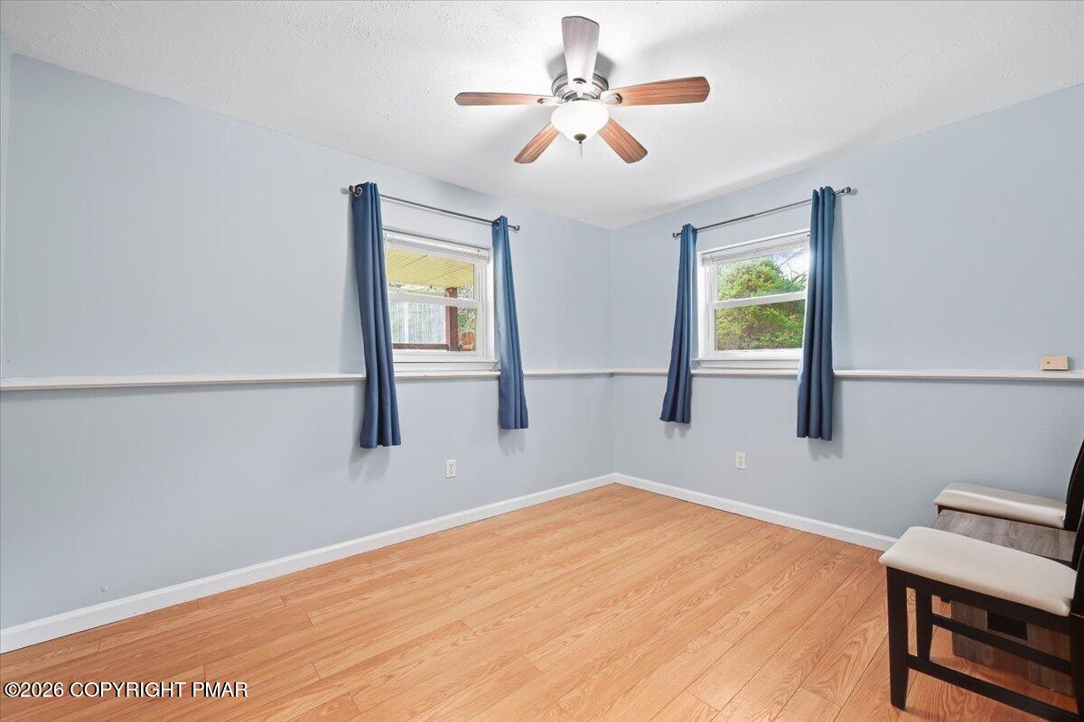 Room with pale blue walls, wood flooring, two curtained windows, and a ceiling fan.