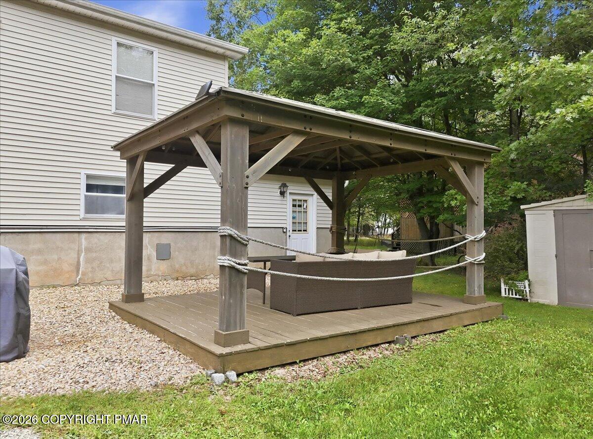 Wooden backyard pavilion with a raised deck, covered seating area, and trees behind the house.