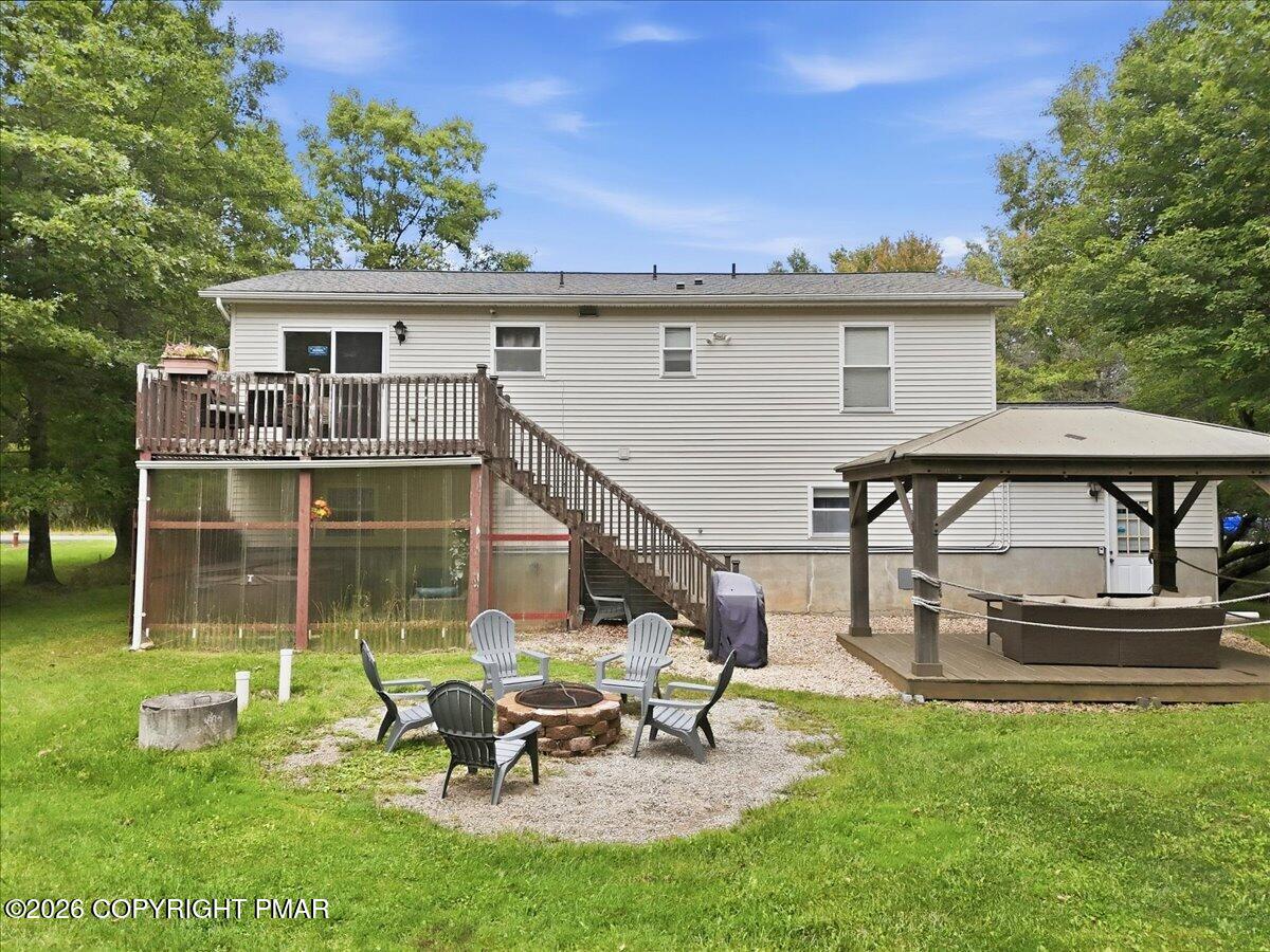 Rear of a light-colored house with a raised deck, gazebo, and gravel fire-pit seating area.