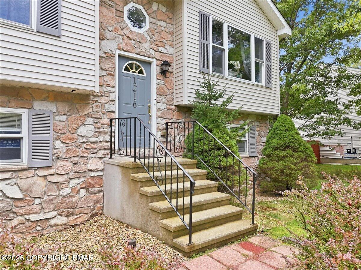 Home entrance with a stone façade, gray door marked 1216, and concrete steps with black railings.