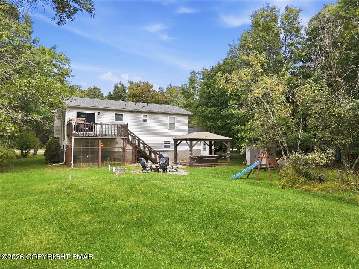 House rear with raised deck, gazebo, broad lawn, and children's play equipment among trees.