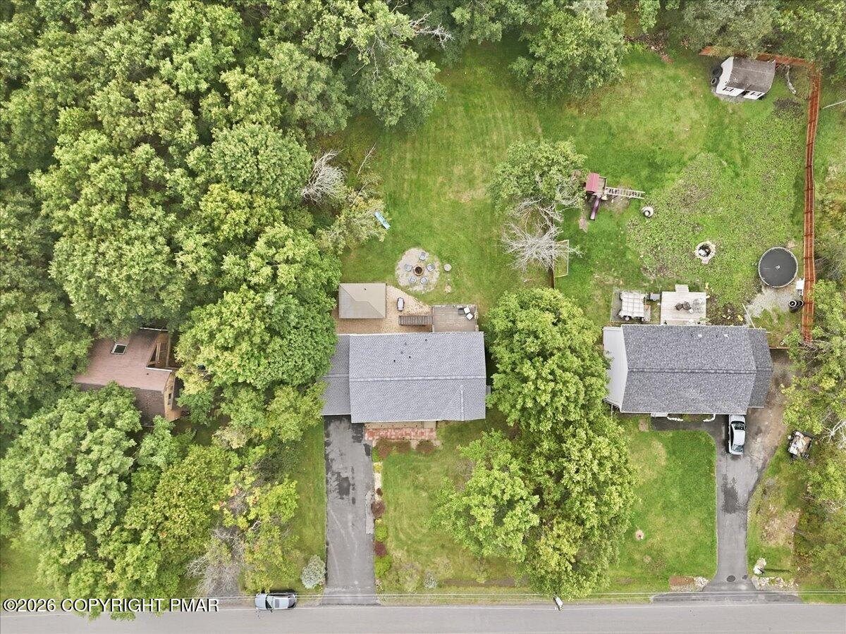 Aerial view of a home surrounded by mature trees, with a large lawn and fire pit.