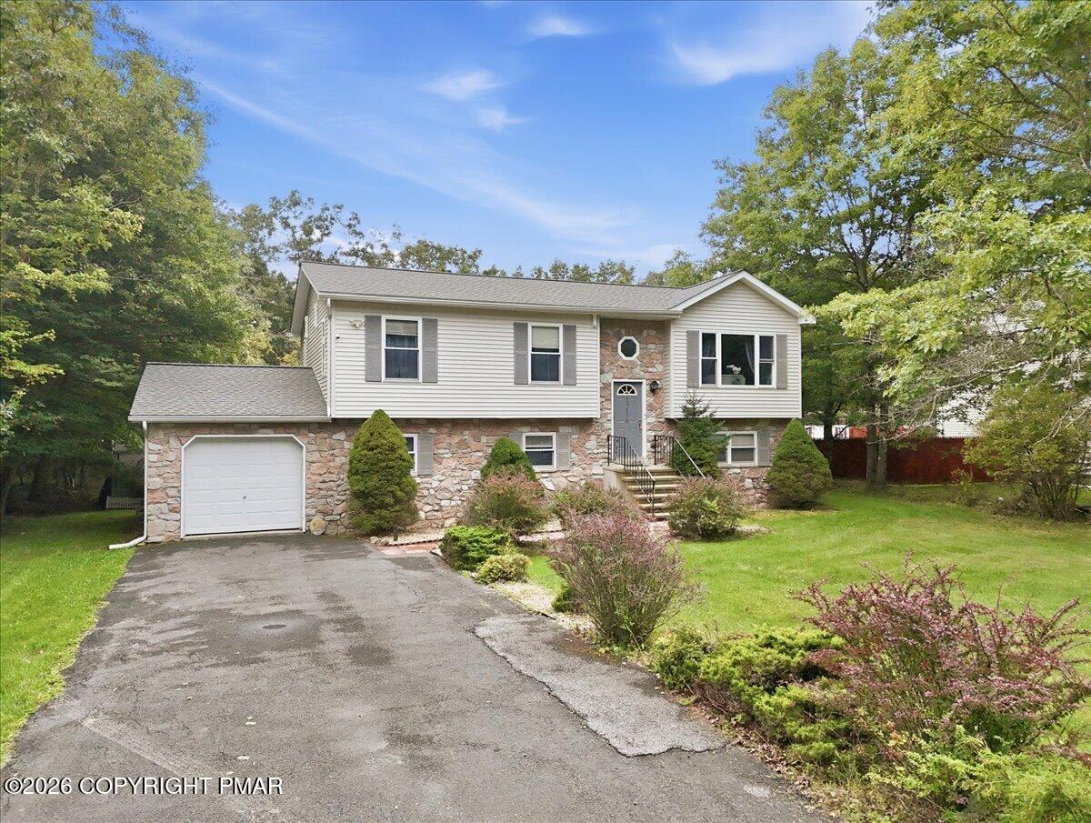 Split-level house with a stone facade, attached garage, paved driveway, and landscaped lawn.