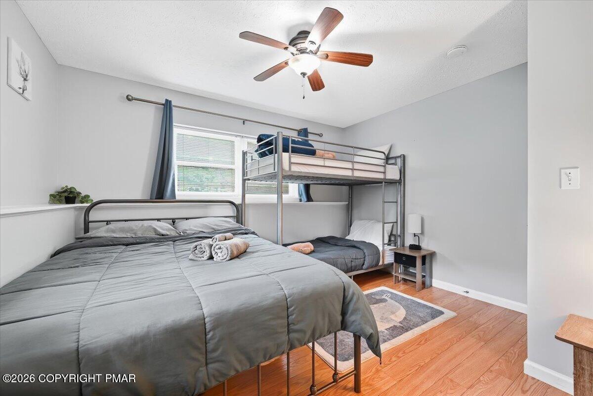 Bedroom with a large gray bed, metal bunk bed, ceiling fan, and hardwood floors.