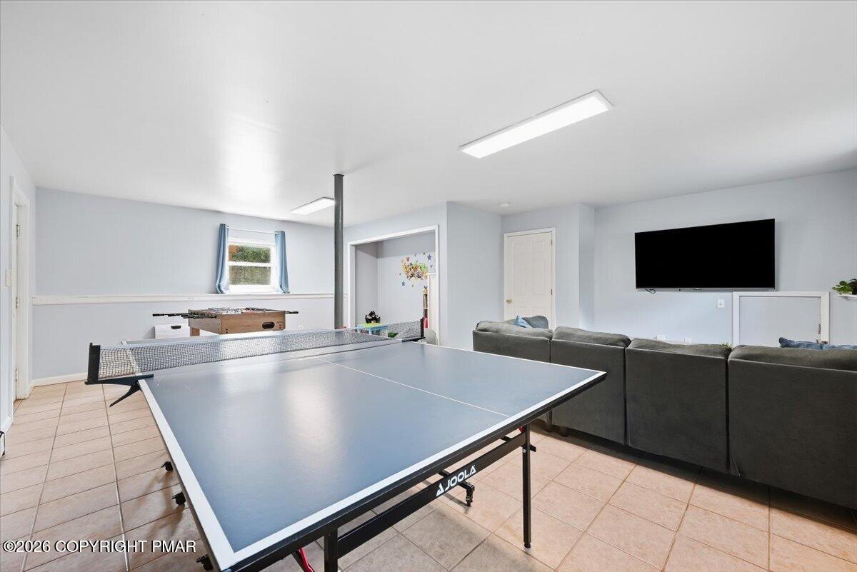 Recreation room with a large ping-pong table, foosball table, sectional sofa, and wall-mounted television.