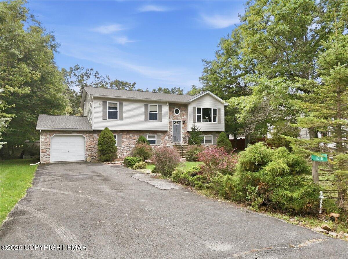 Split-level house with stone accents, attached garage, and landscaped front yard.