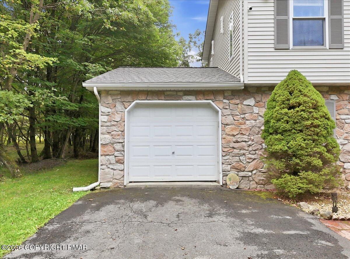 Attached garage with a stone facade, cracked driveway, and mature trees.