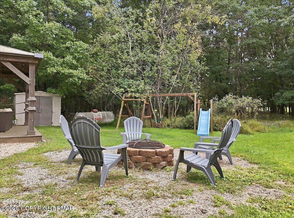 Backyard fire pit with Adirondack chairs, a swing set and blue slide among the trees.