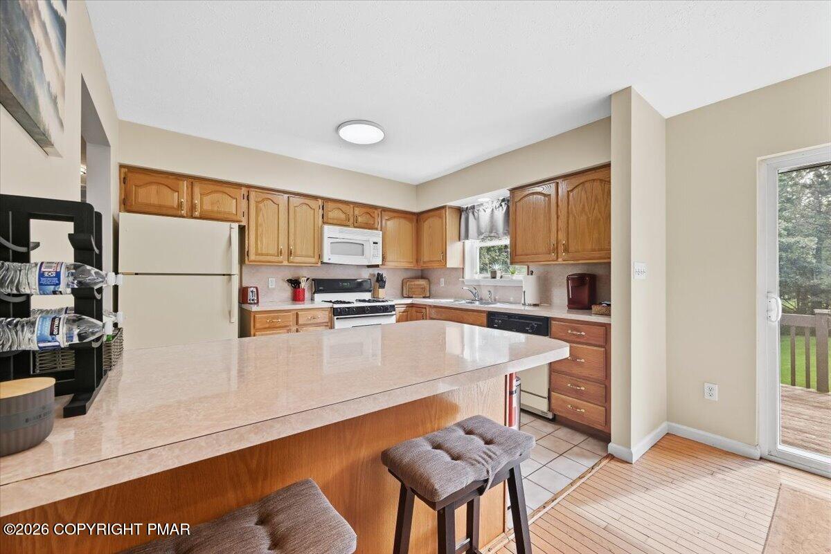 Kitchen with wood cabinets, a large countertop peninsula, upholstered stools, and a sliding glass door to the deck.