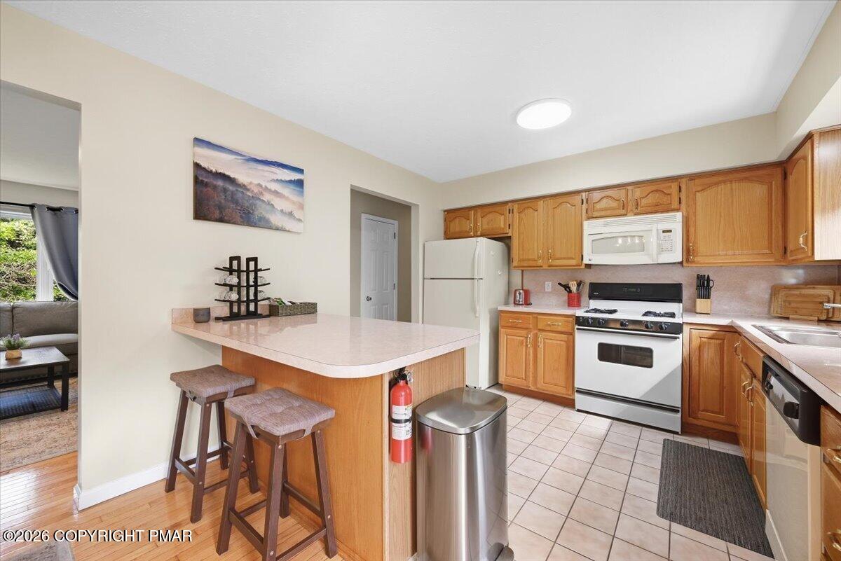 Kitchen with honey-colored cabinets, white appliances, and a peninsula breakfast bar with stools.