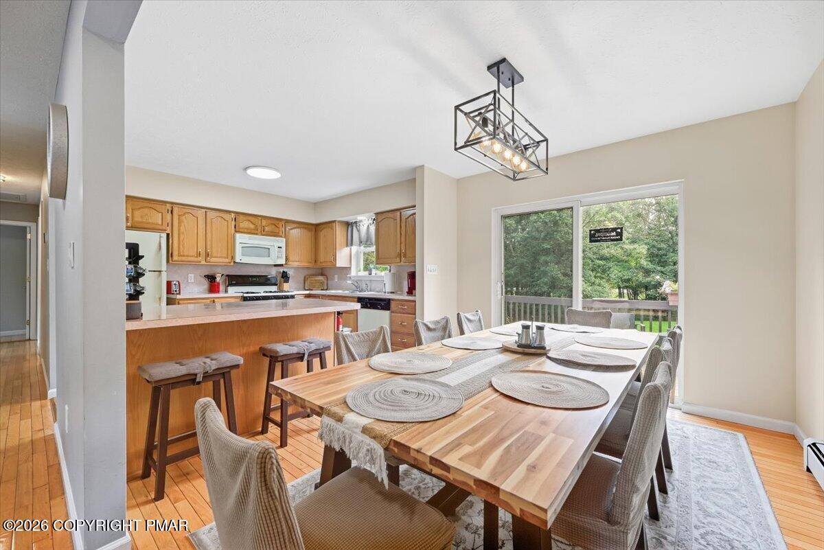 Dining area with a long set table beside a wood-cabinet kitchen and sliding door to a leafy deck.