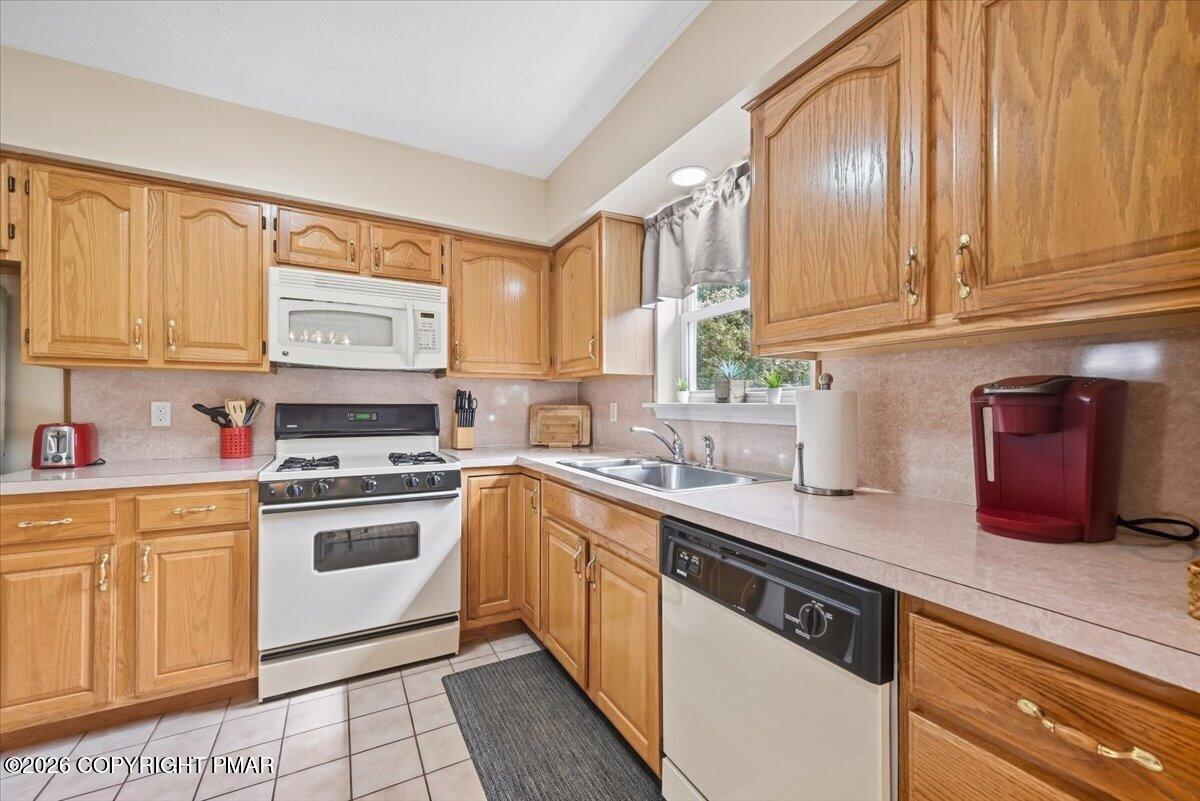 Kitchen with honey-colored wood cabinets, a white gas range, and a sink beneath a window.