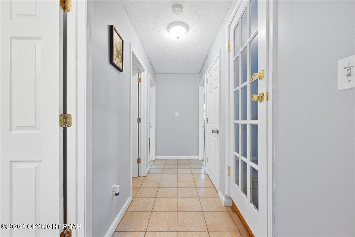 Hallway with tan tile flooring, gray walls, and a white glass-paneled door.