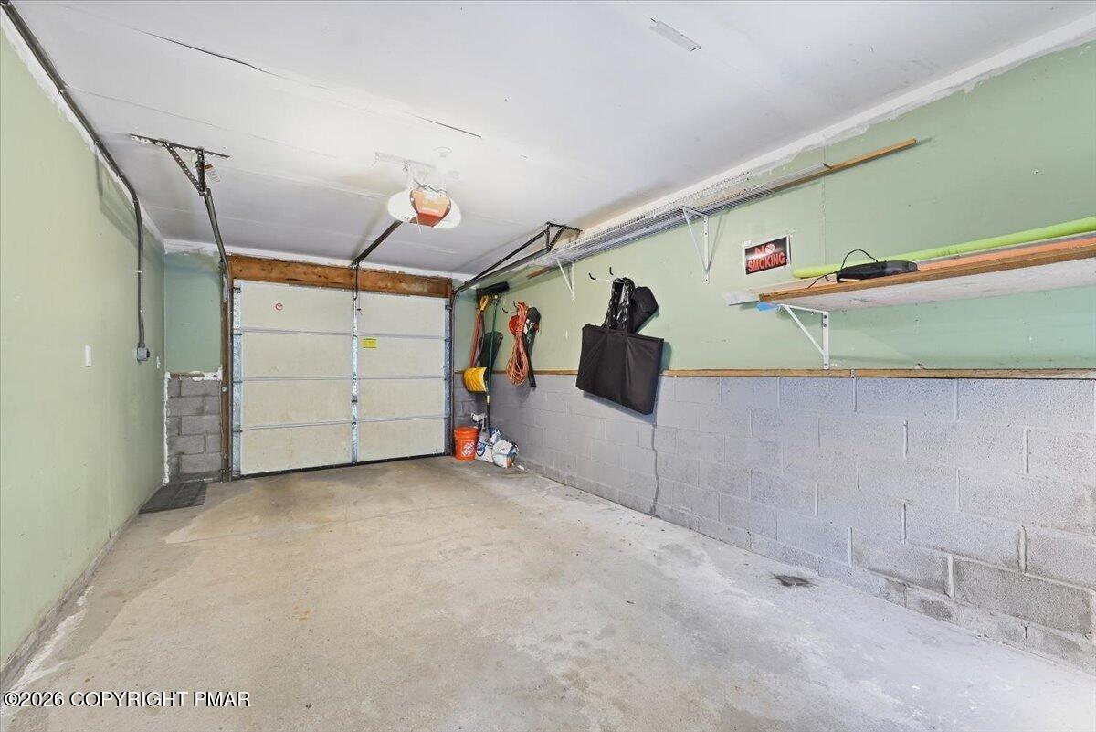 Garage with a closed sectional door, concrete floor, and storage shelves along the wall.