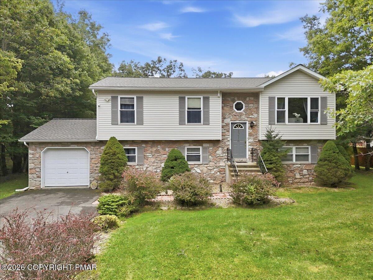 Split-level house with stone veneer, white siding, an attached garage, and a landscaped front lawn.
