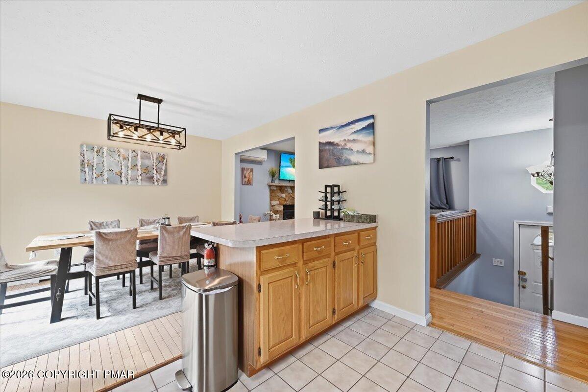 Kitchen and dining area with honey-colored cabinets, tiled flooring, and a geometric pendant light.