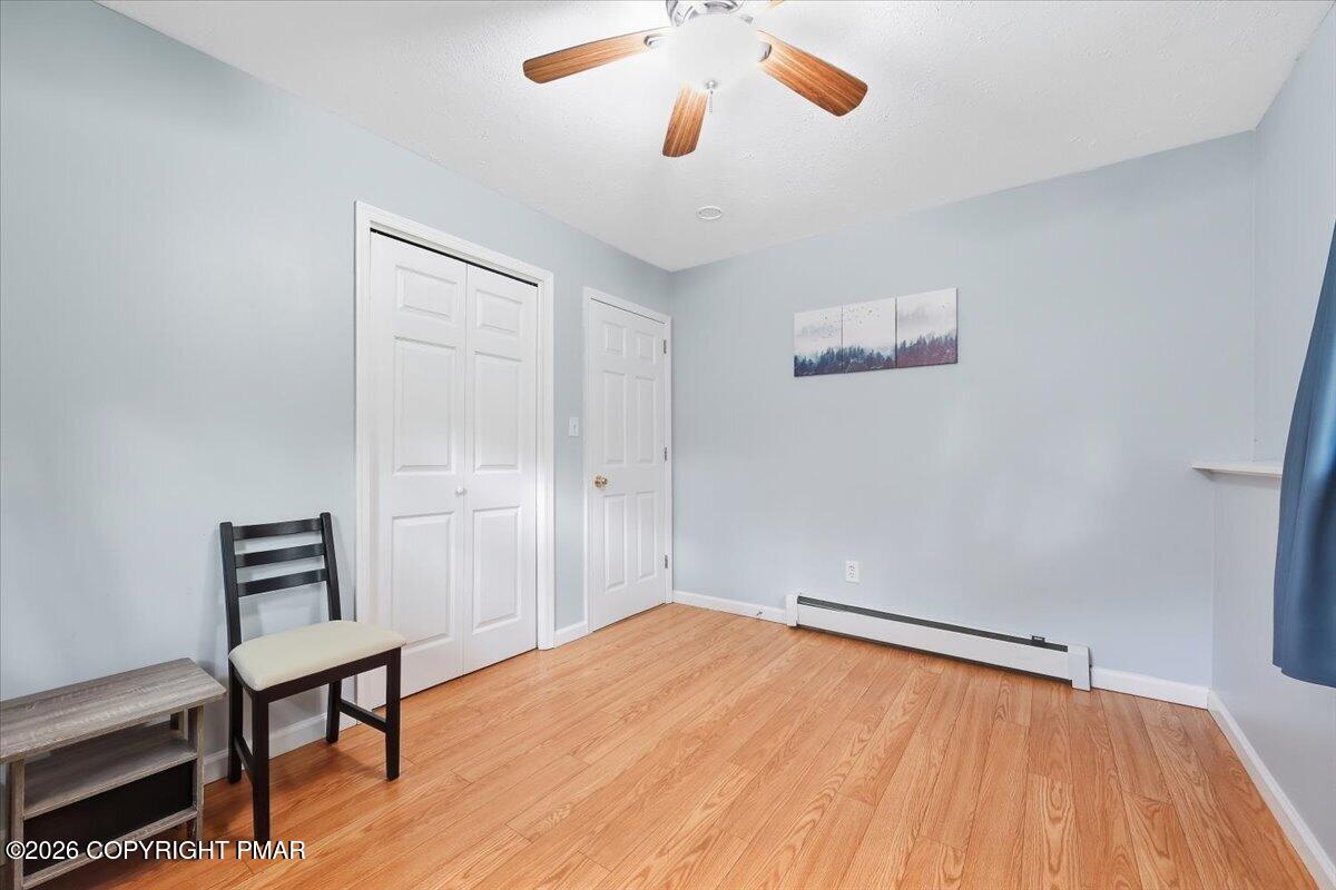 Room with wood flooring, white closet doors, a ceiling fan, and a chair.