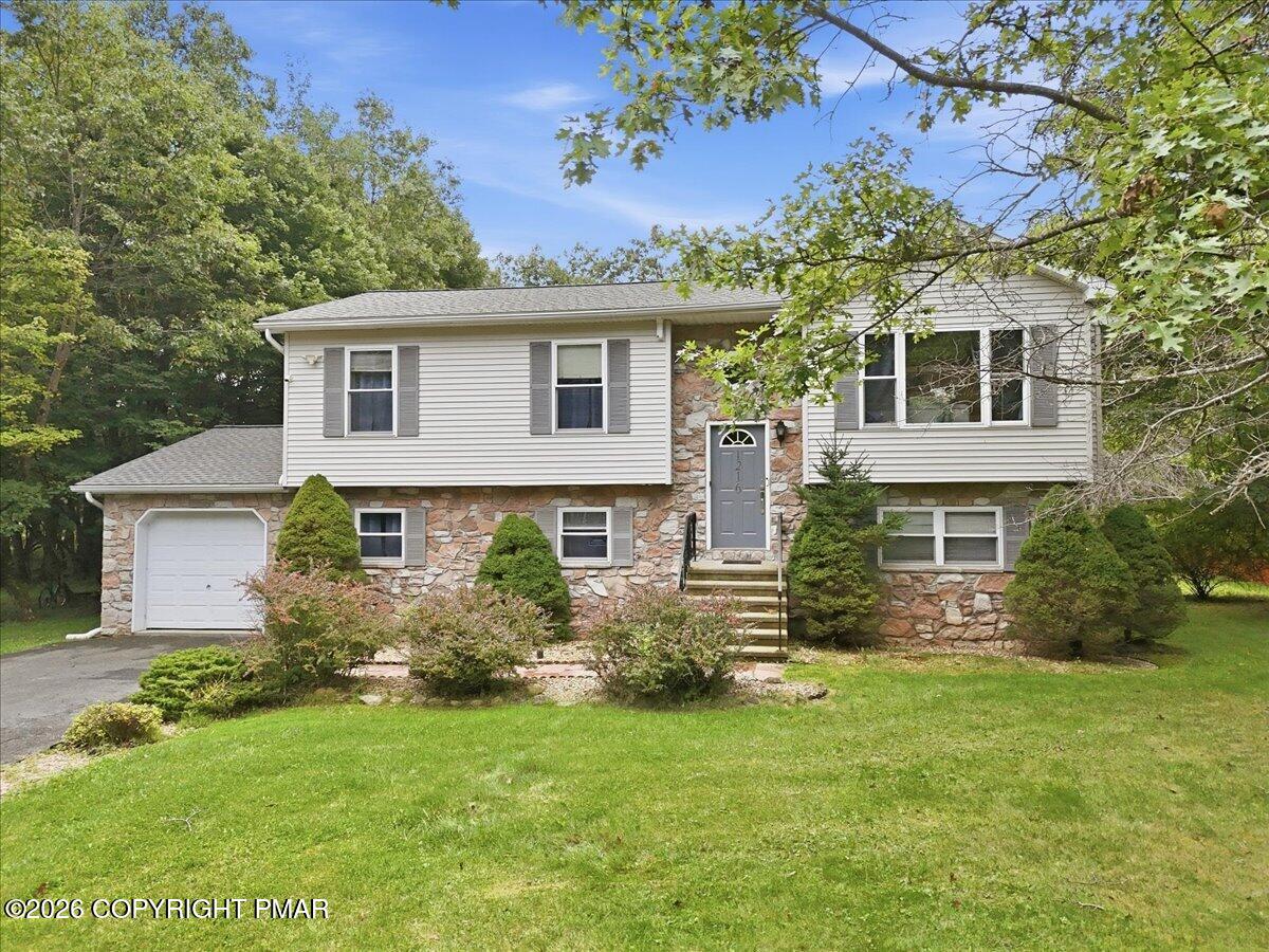Split-level home with a stone façade, attached garage, landscaped shrubs, and a broad green lawn.