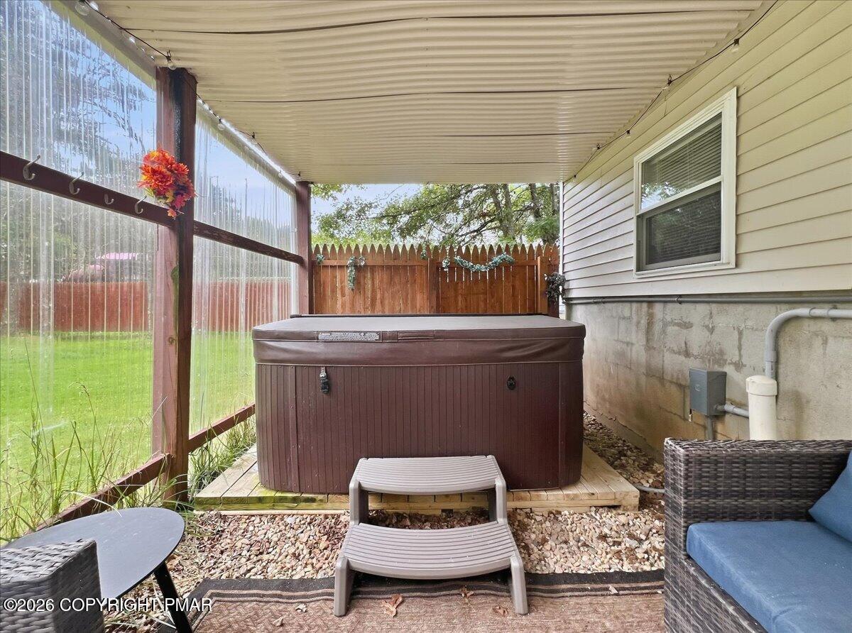 Covered patio with a large hot tub, wicker seating, and a wooden privacy fence.