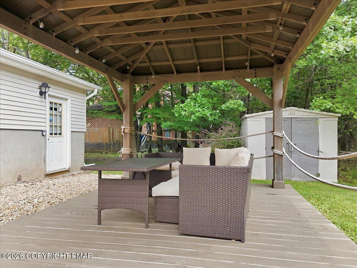 Covered backyard deck with timber pavilion and wicker seating beside a wooded yard.