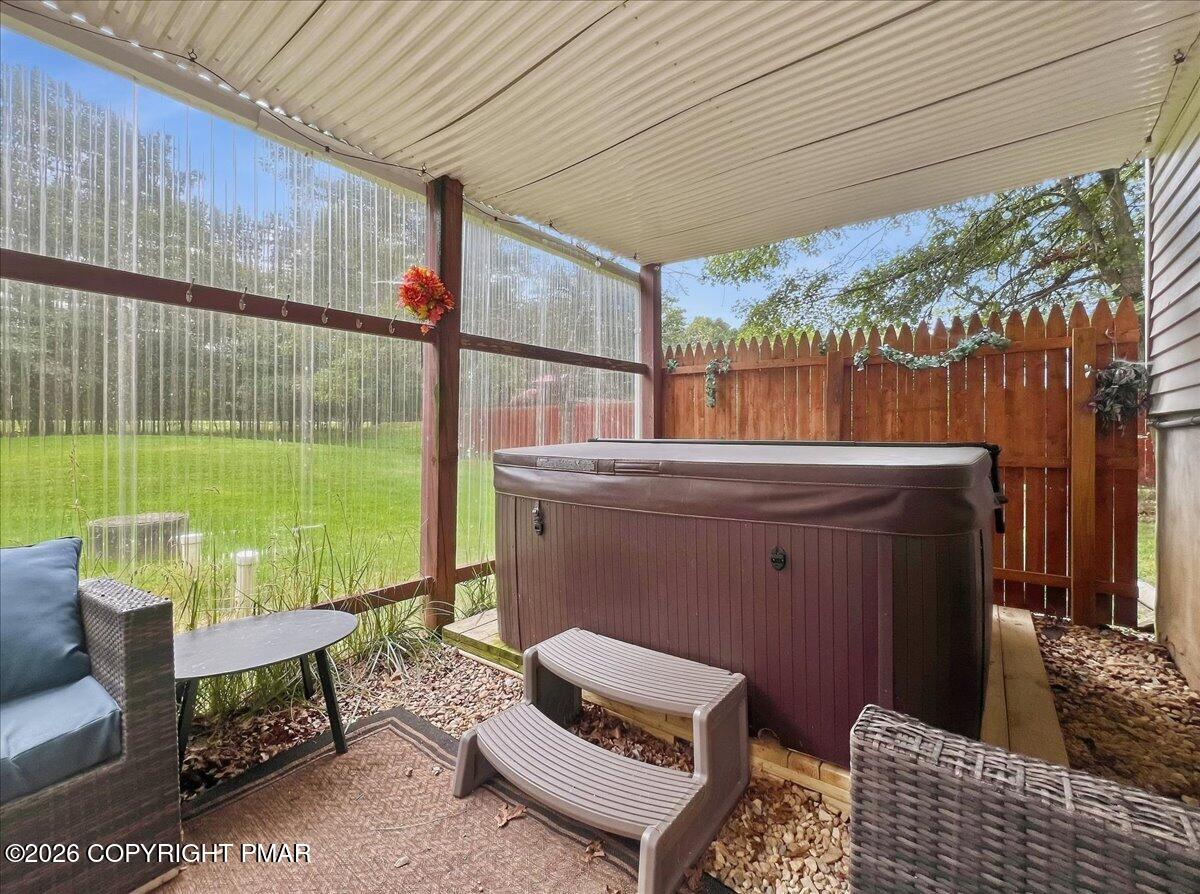 Covered patio with a hot tub, wicker seating, and a fenced yard beyond.