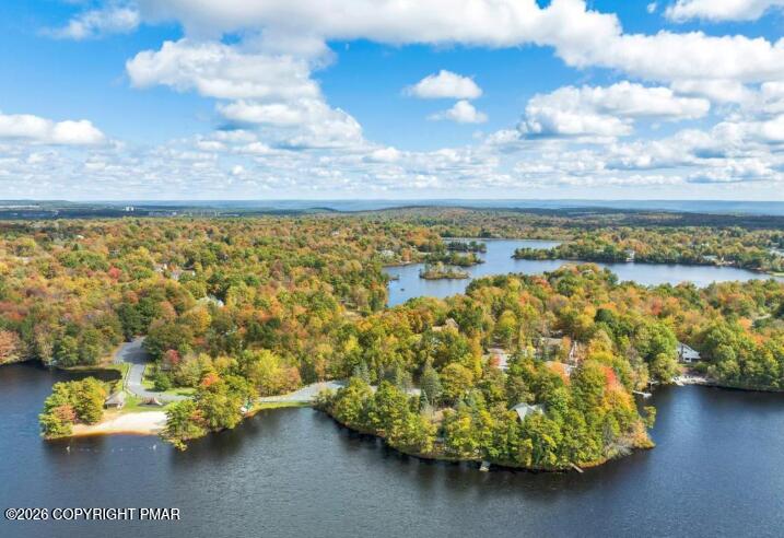 Aerial view of autumn-colored woods and homes along a lake.