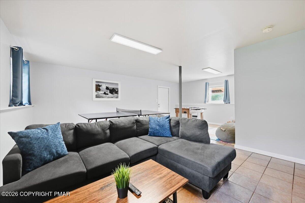 Recreation room with a gray sectional sofa, ping-pong table, and tiled floor.