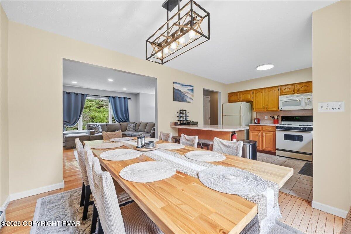 Open-plan dining room with a long wooden table beside a kitchen with honey-colored cabinets and a gray sectional.