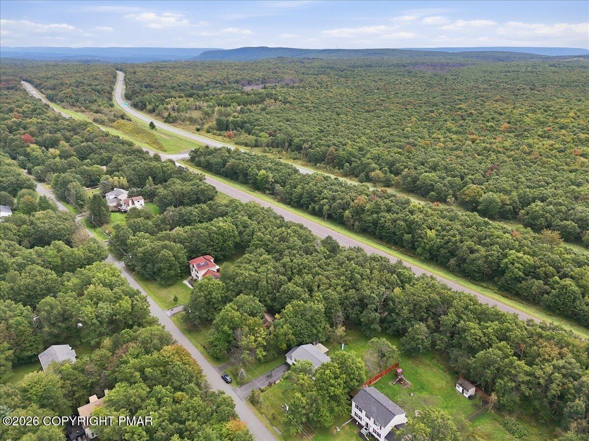 Aerial view of homes among wooded hills, with a highway and distant ridges.