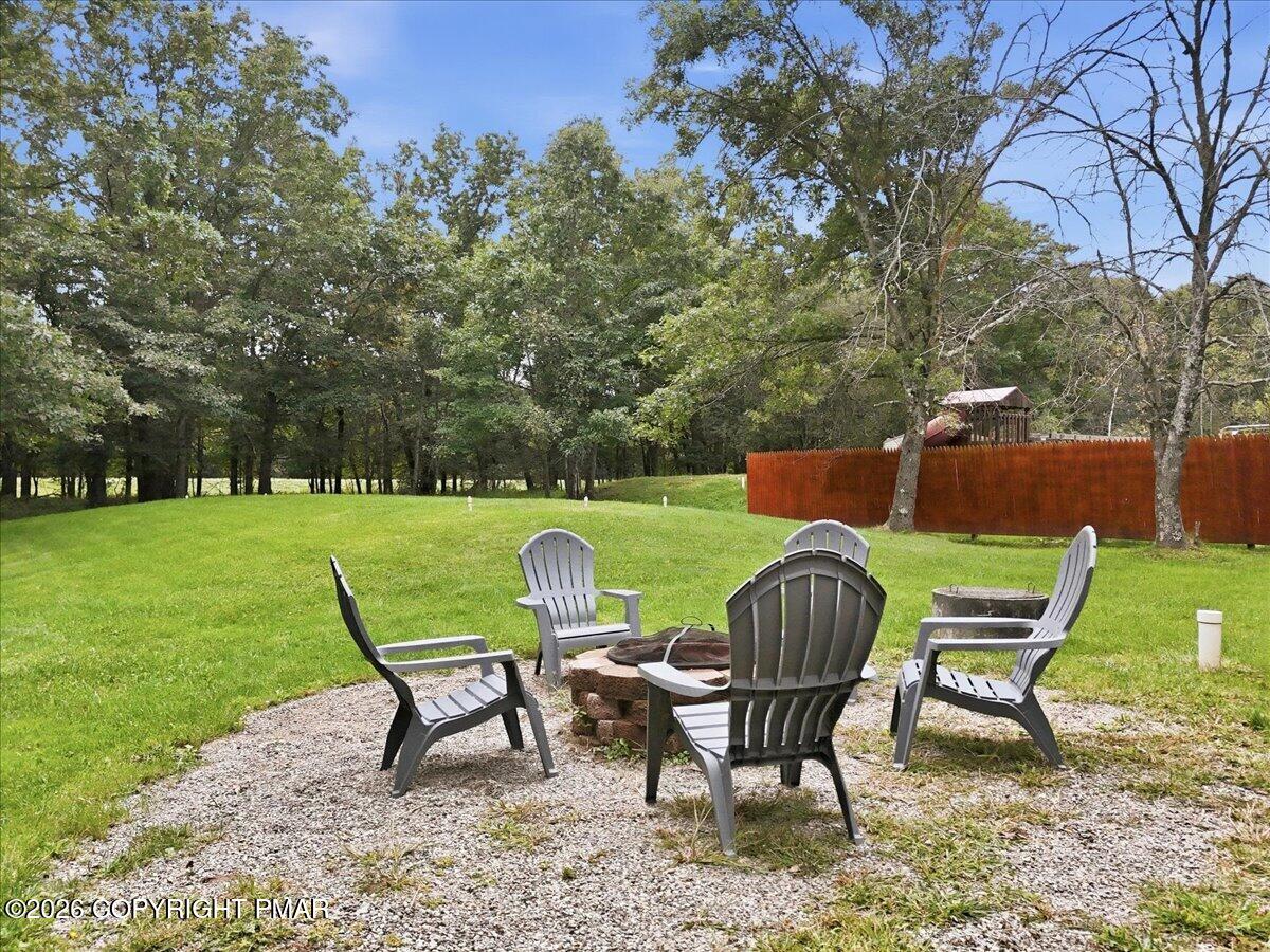 Backyard patio with Adirondack chairs around a fire pit, overlooking a green lawn and mature trees.