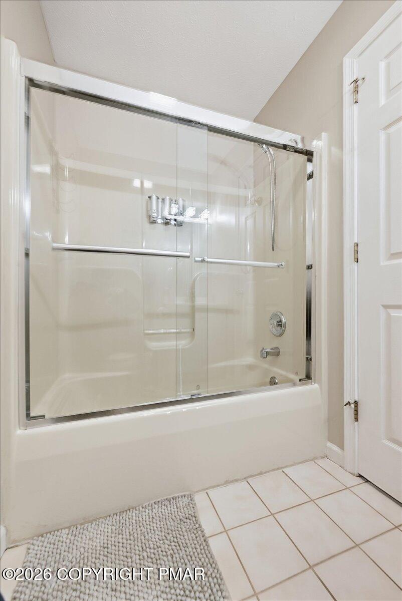 Bathroom bathtub with clear sliding glass doors, chrome fixtures, and white tile flooring.