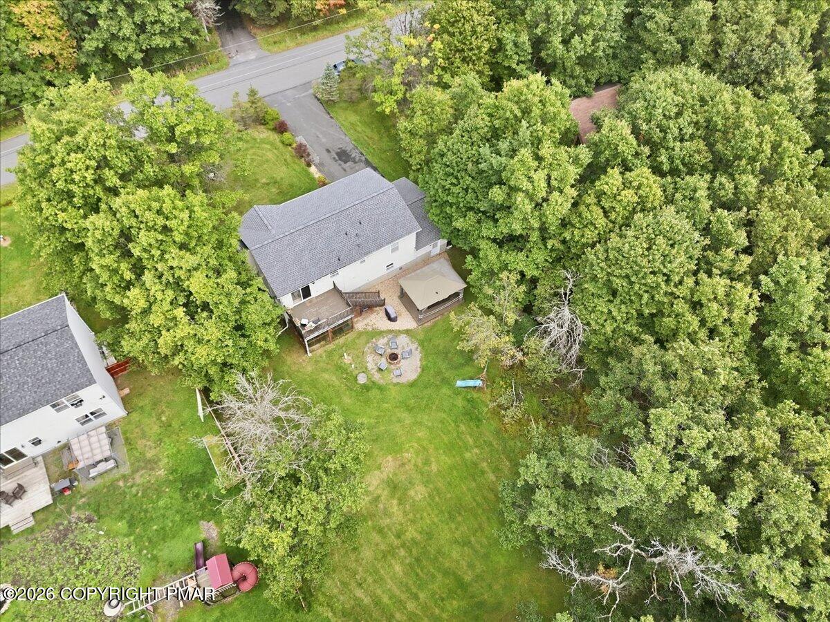 Aerial view of a white house surrounded by trees, with a large lawn and backyard fire pit.