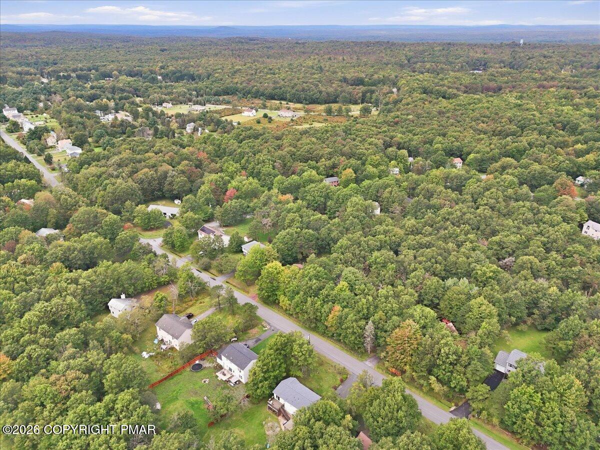 Aerial view of a wooded neighborhood with scattered homes and roads amid early autumn foliage.