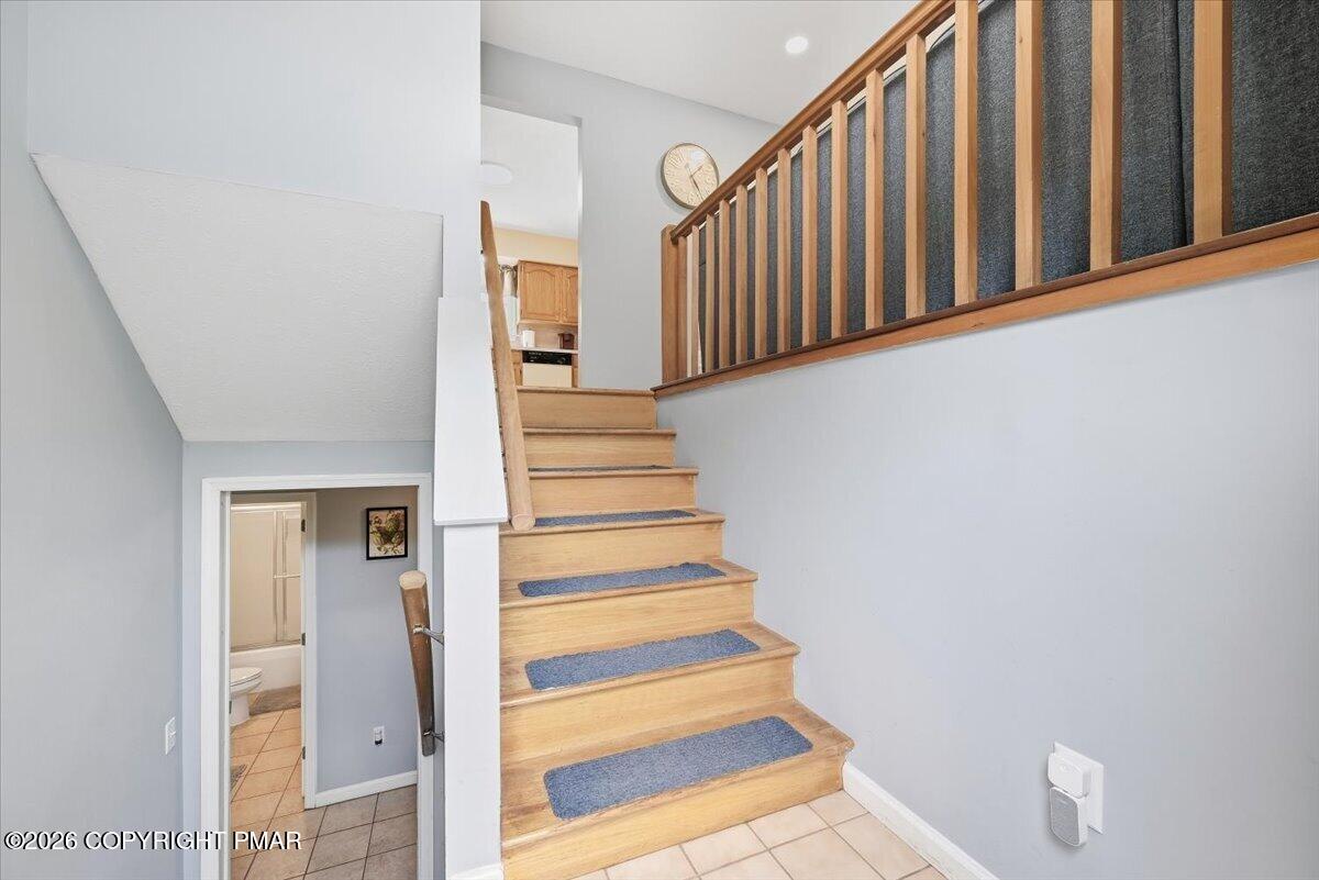 Light wood staircase with blue carpet treads and wood railing; tiled floor and bathroom doorway below.