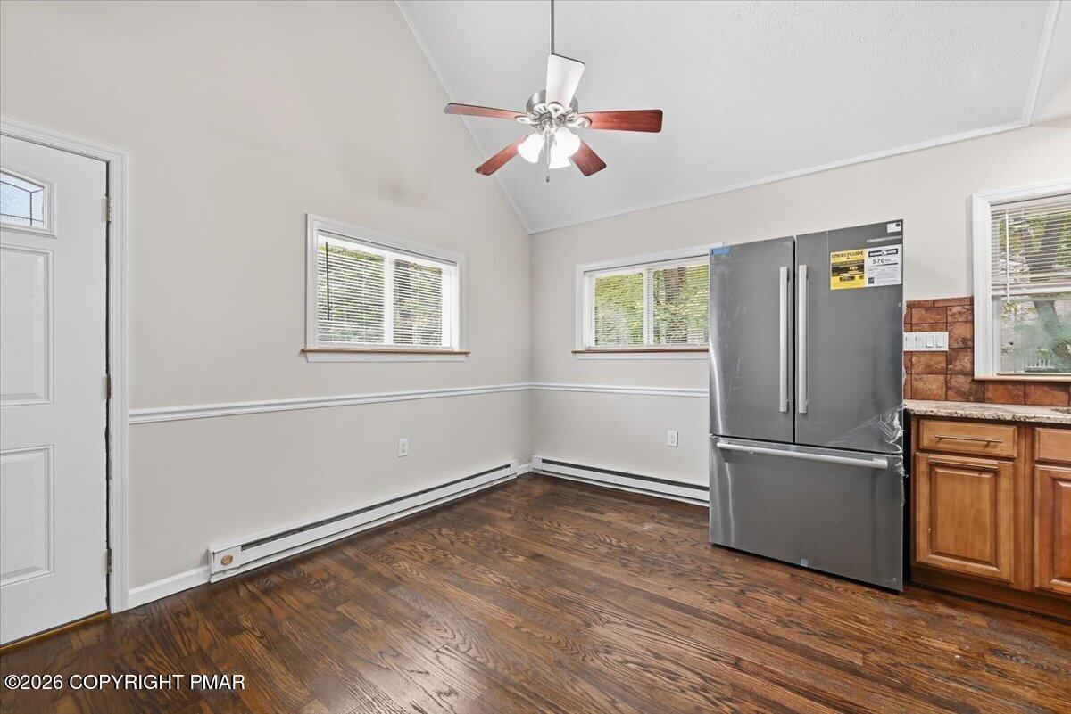 Unfurnished kitchen with dark hardwood floors, a stainless-steel refrigerator, and wood cabinets.