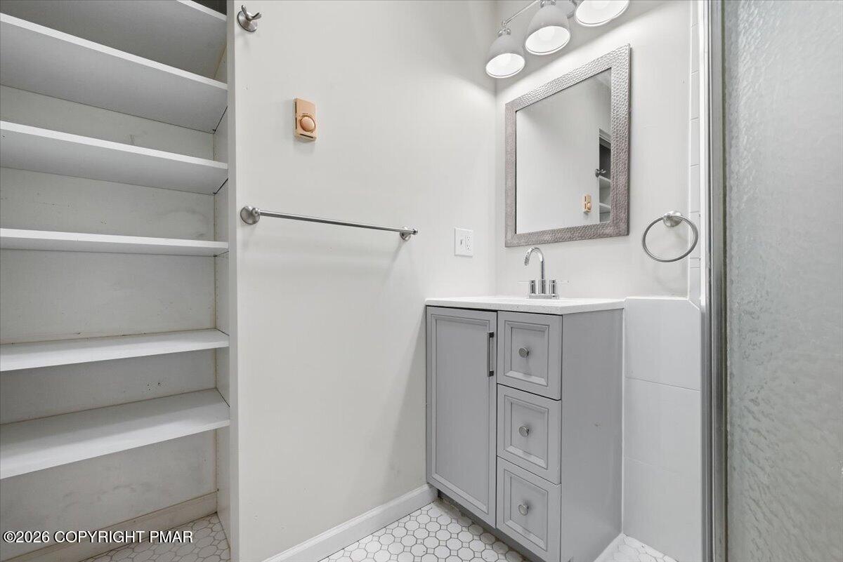 Bathroom with gray vanity, open built-in shelves, and white hexagonal tile floor.