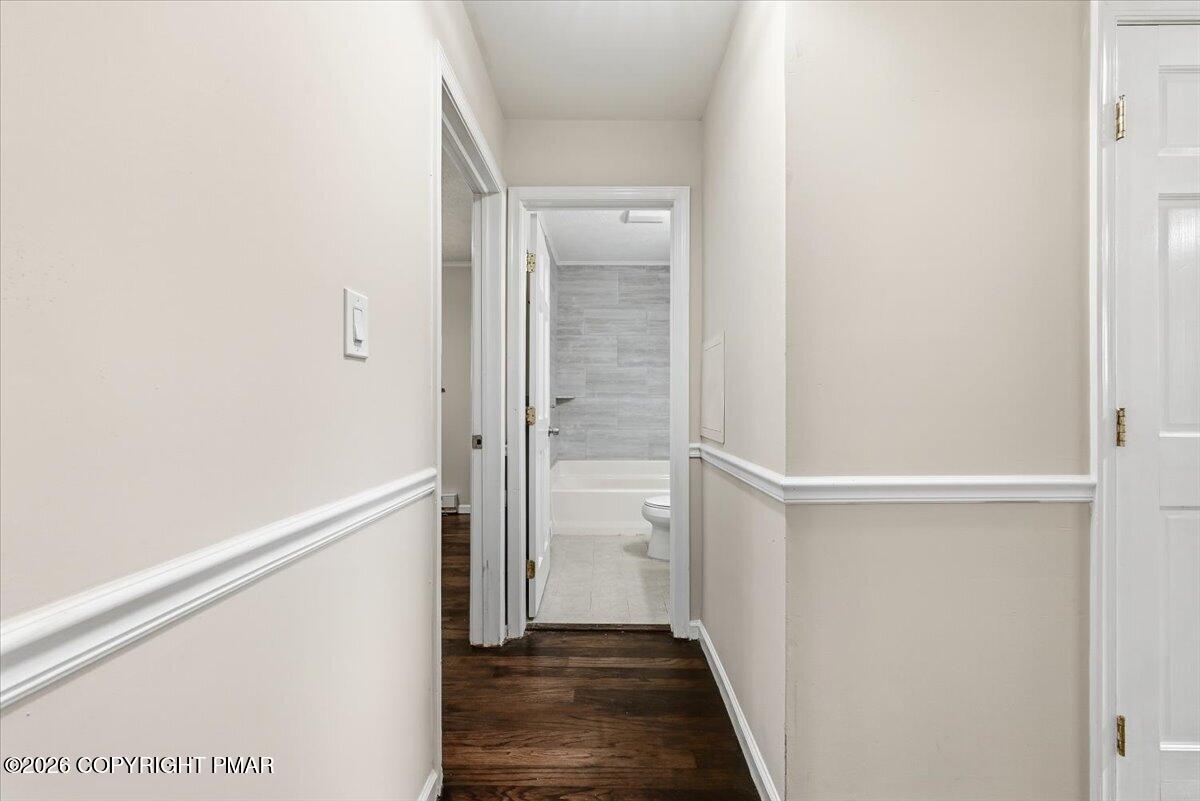 Hallway with dark wood floors and chair rail leading to a tiled bathroom with a bathtub.