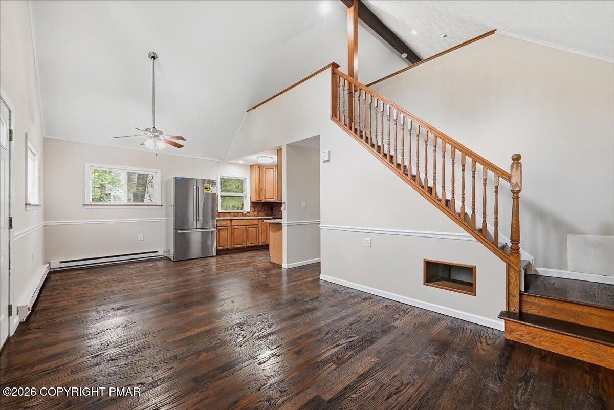 Open living area with dark hardwood floors, vaulted ceiling, and staircase beside a compact kitchen.
