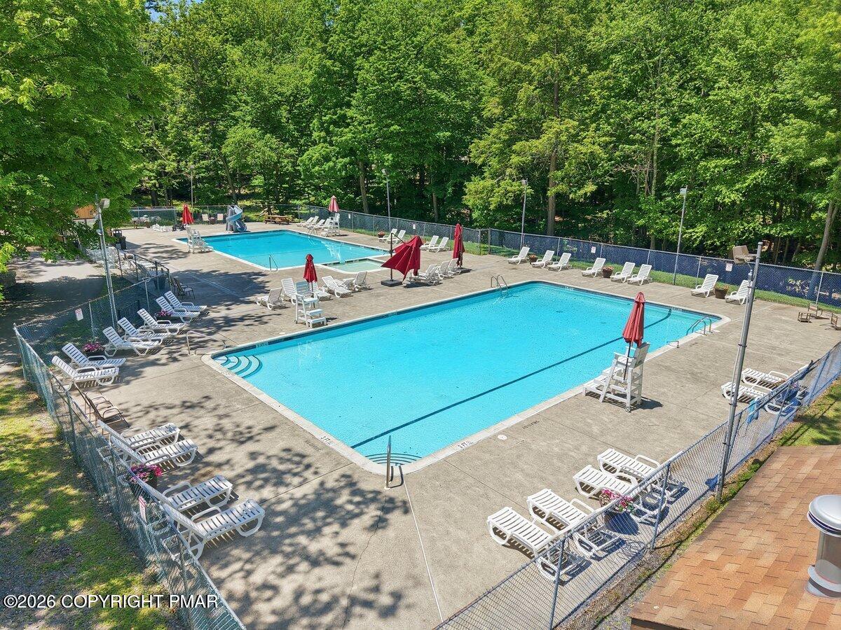 Two outdoor swimming pools with lounge chairs and red umbrellas, surrounded by trees.