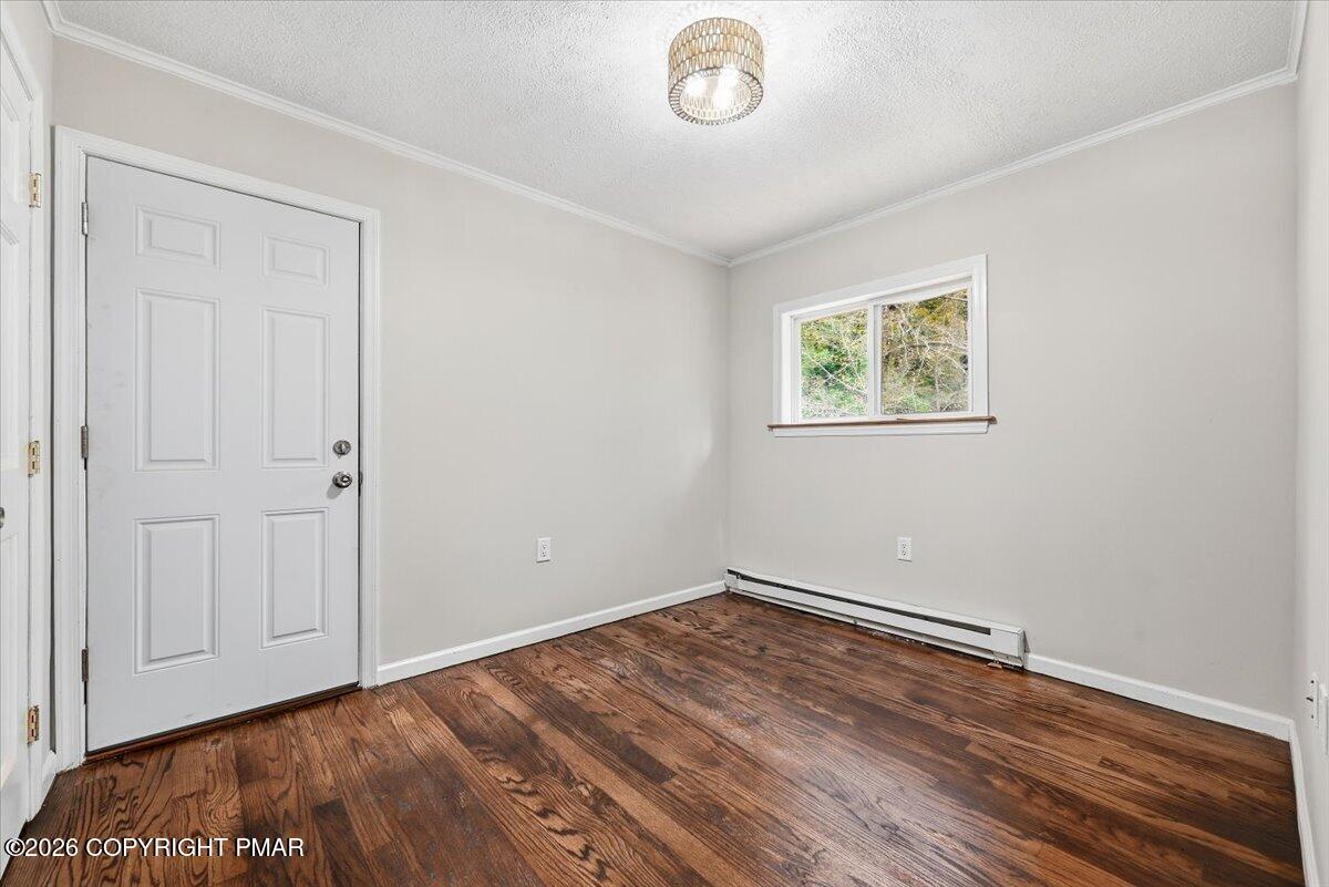 Empty room with dark hardwood floors, a white paneled door, and a small window.