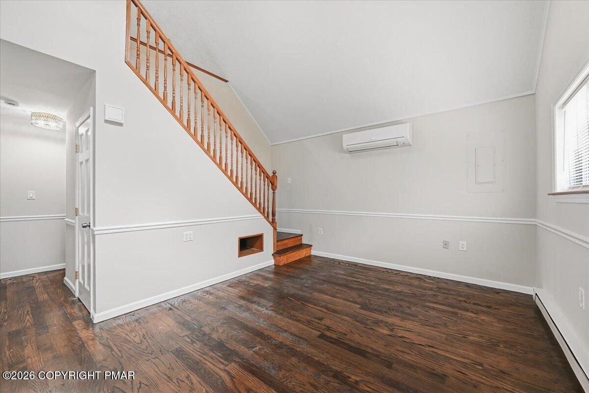 Unfurnished living room with dark wood floors, a wooden staircase, and a wall-mounted mini-split air conditioner.