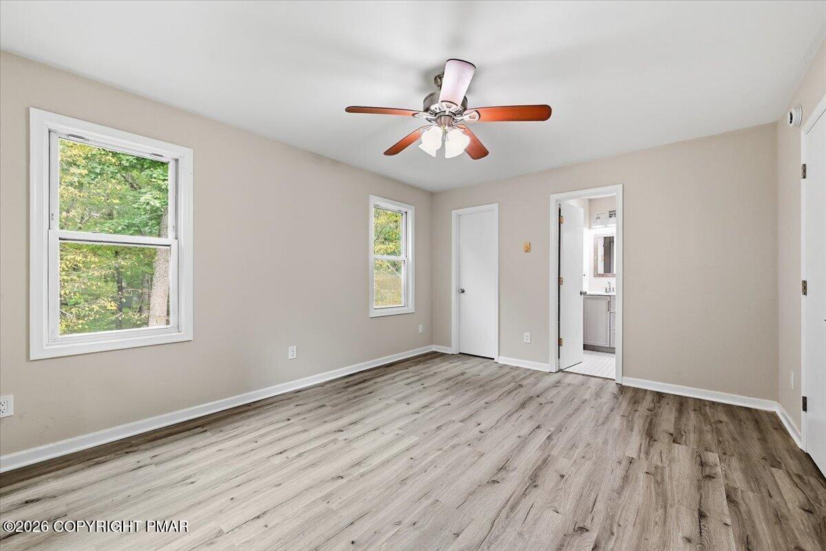 Empty room with gray wood-look flooring, two windows, and a ceiling fan.