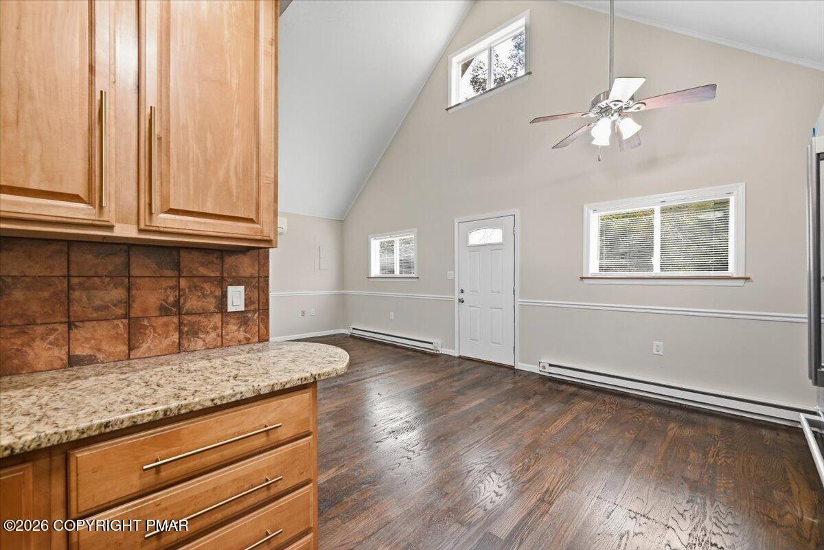 Kitchen with wood cabinetry and granite counter opening to a vaulted, empty living area.