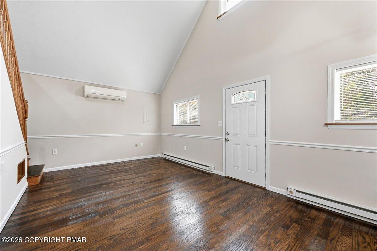Empty room with dark hardwood floors, a high sloped ceiling, and a white entry door.