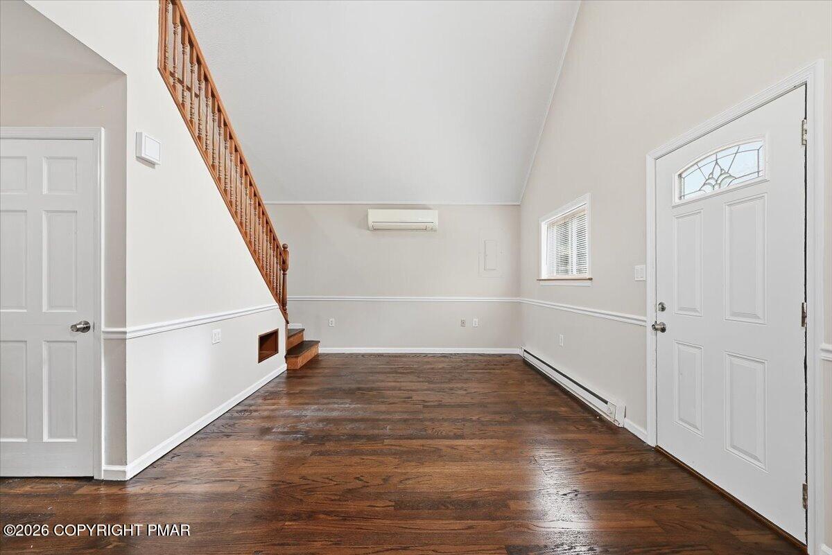 Unfurnished entry room with dark hardwood floors, a wooden staircase, and a white front door.